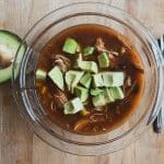 bowl of soup on a wood table with avocado on top