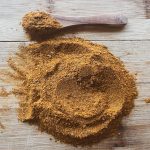 shawarma seasoning in a mound on a wood table iwth wooden spoon next to it