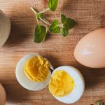four eggs on a wooden table, one cut open to expose the yolk