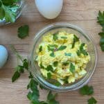 egg salad in a glass bowl with farm fresh eggs and parsley bordering the dish