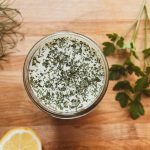 homemade ranch dressing on a wood surface with some herbs and a lemon