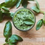 glass jar of easy homemade basil pesto with a wooden spoon and some basil leaves around it