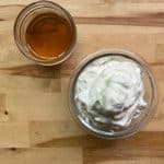 glass bowl of easy homemade whipped cream on a wooden surface with a cup of maple syrup to the left