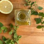 greek dressing in a scotch bottle with half a lemon and fresh oregano around it