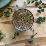 homemade oregano oil on a wood surface with fresh oregano spread about