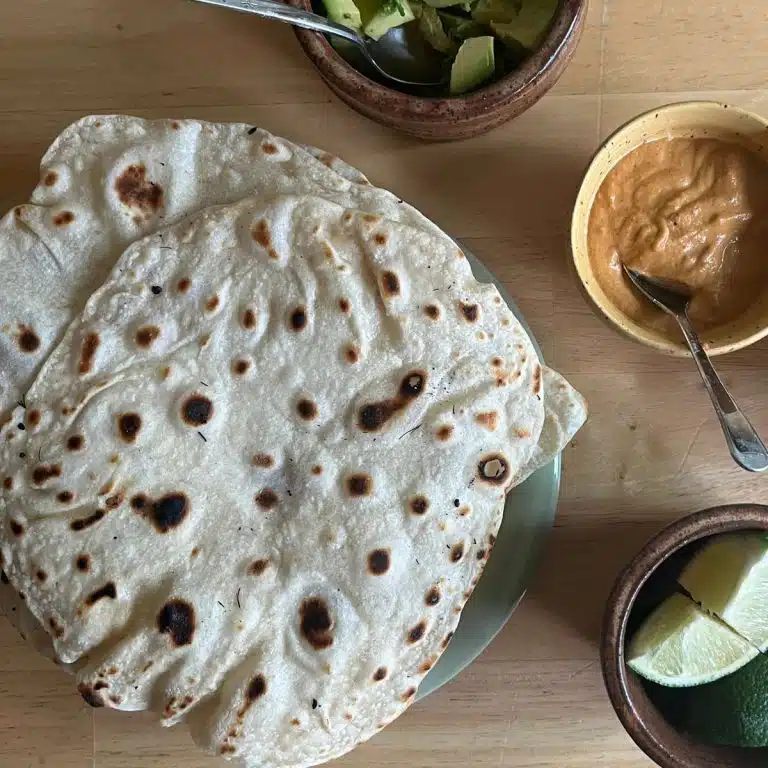 homemade flour tortillas on a wood table with avocado, lime, sauce